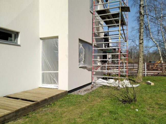 Isolement de façade d’une maison moderne Façade d’une maison en rénovation, avec des échafaudages installés et des fenêtres protégées par des bâches plastiques pour des travaux de peinture ou de lavage des murs.