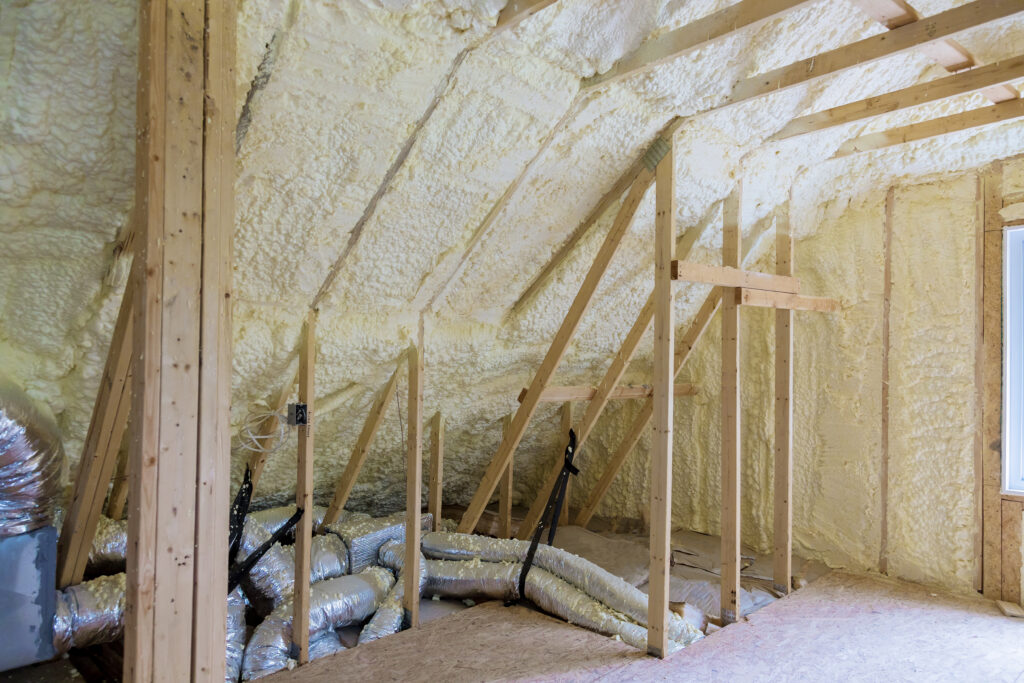 Combles en cours d’aménagement, avec charpente en bois et isolation en mousse projetée sur les murs et le plafond, montrant l’installation du système de ventilation.